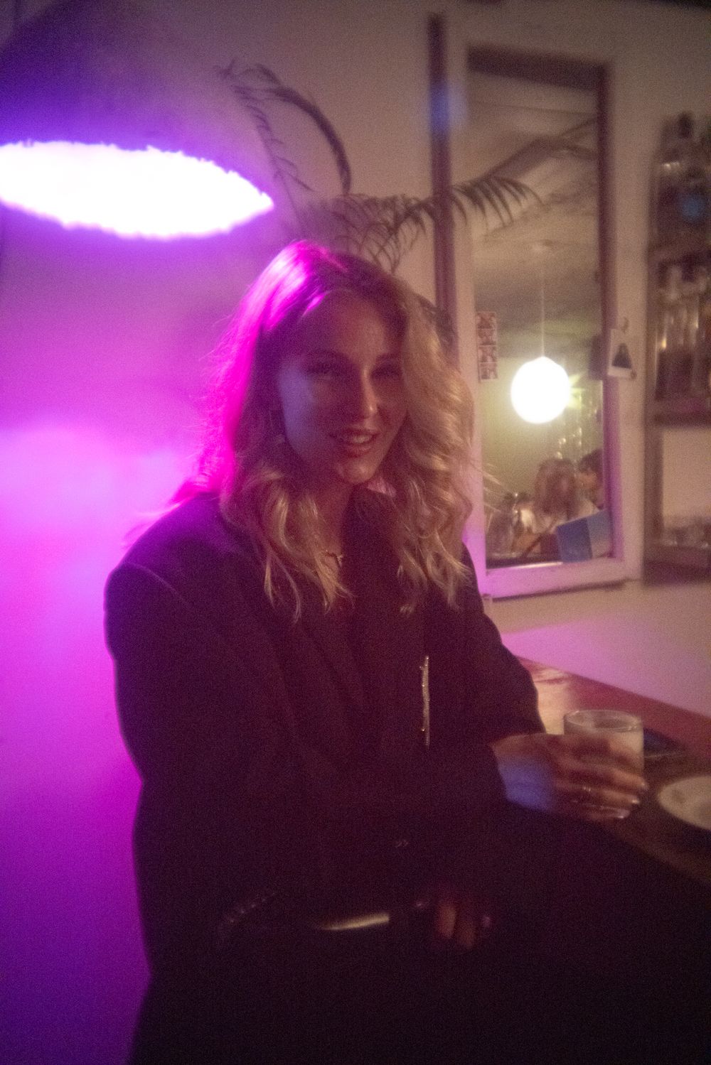 A person sits in a dimly lit room illuminated by vibrant purple lighting from above, creating an atmospheric ambiance.