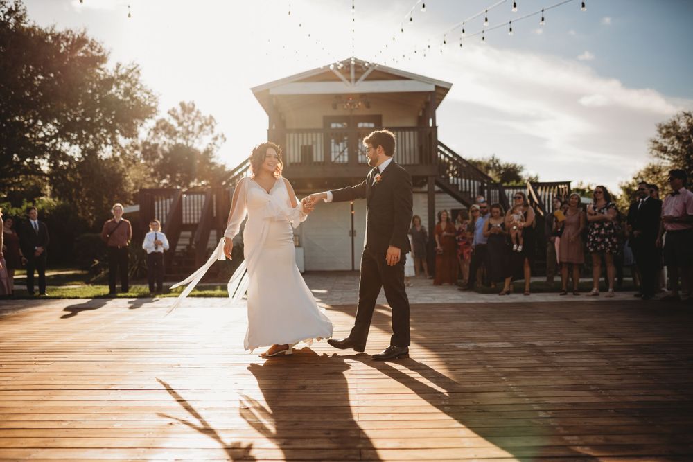 Couple dances on outdoor deck during golden hour with guests watching.