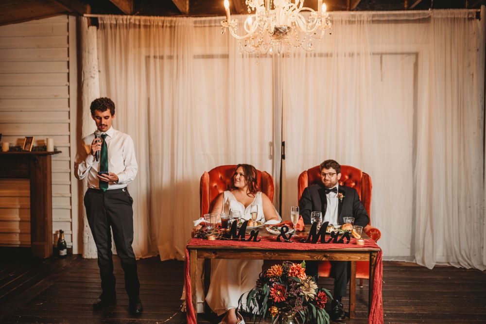 Wedding reception speech at sweetheart table with chandelier overhead.