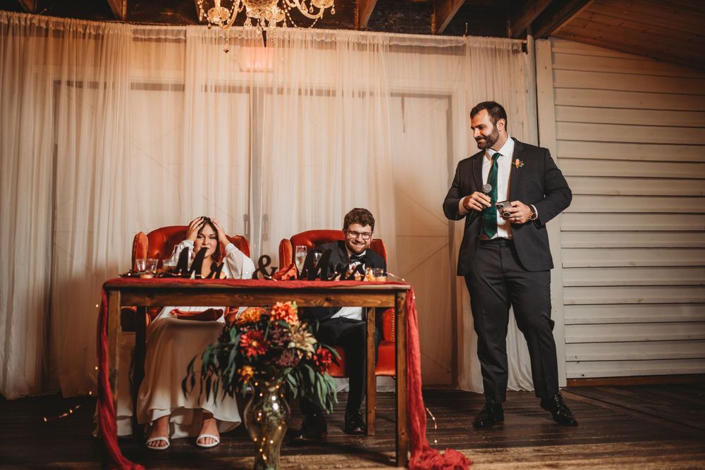 Wedding speaker delivers toast while couple listens at reception table.