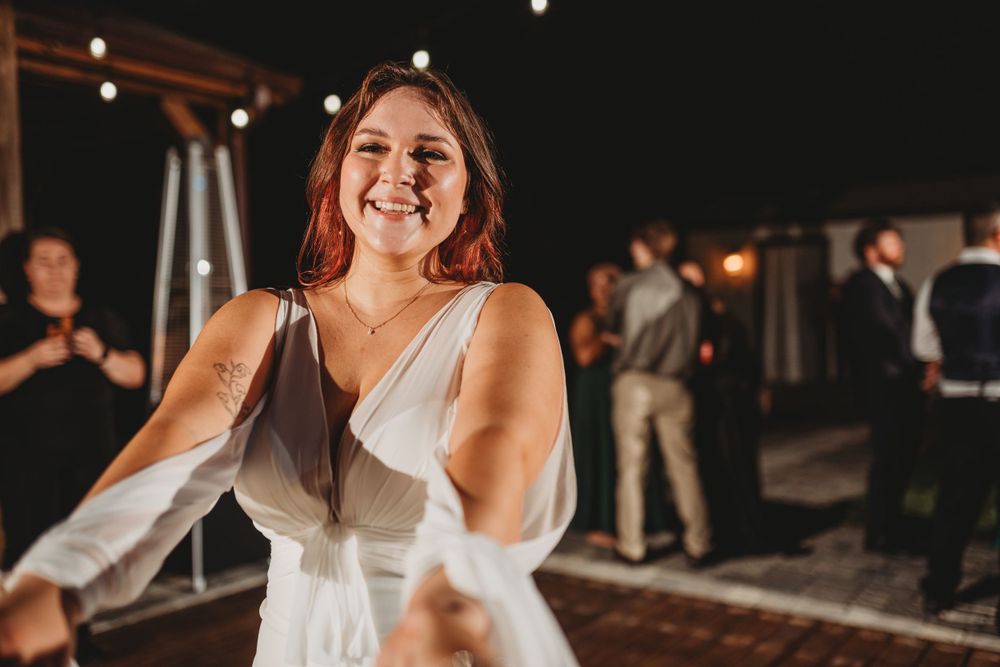 White dress-clad dancer twirls joyfully on a dimly lit outdoor dance floor during an evening celebration.