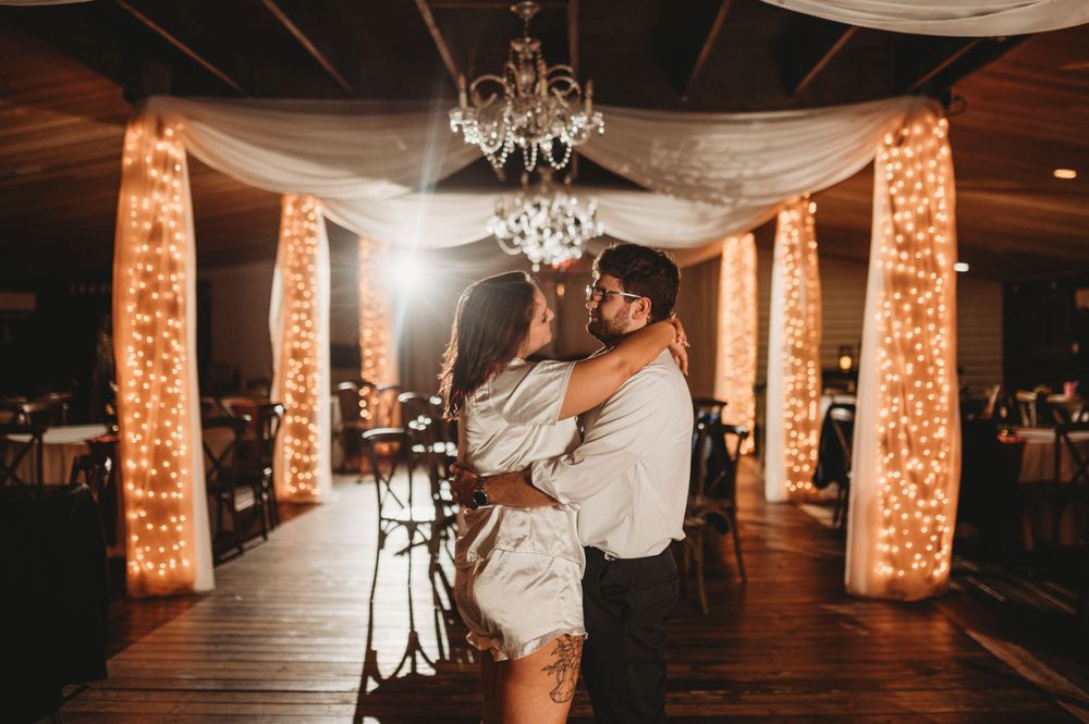 Couple shares intimate dance moment in rustic venue with draped fabric and warm lighting.