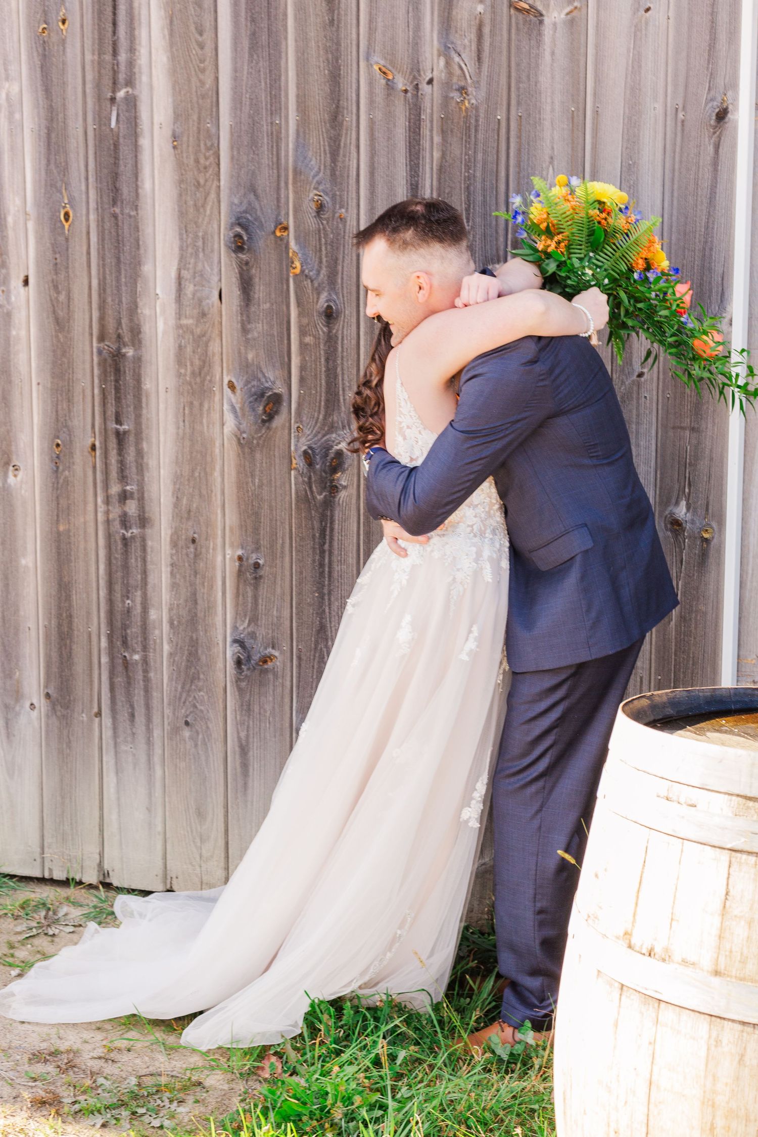 Emotional first look moment against rustic barn wood background with sunflowers.