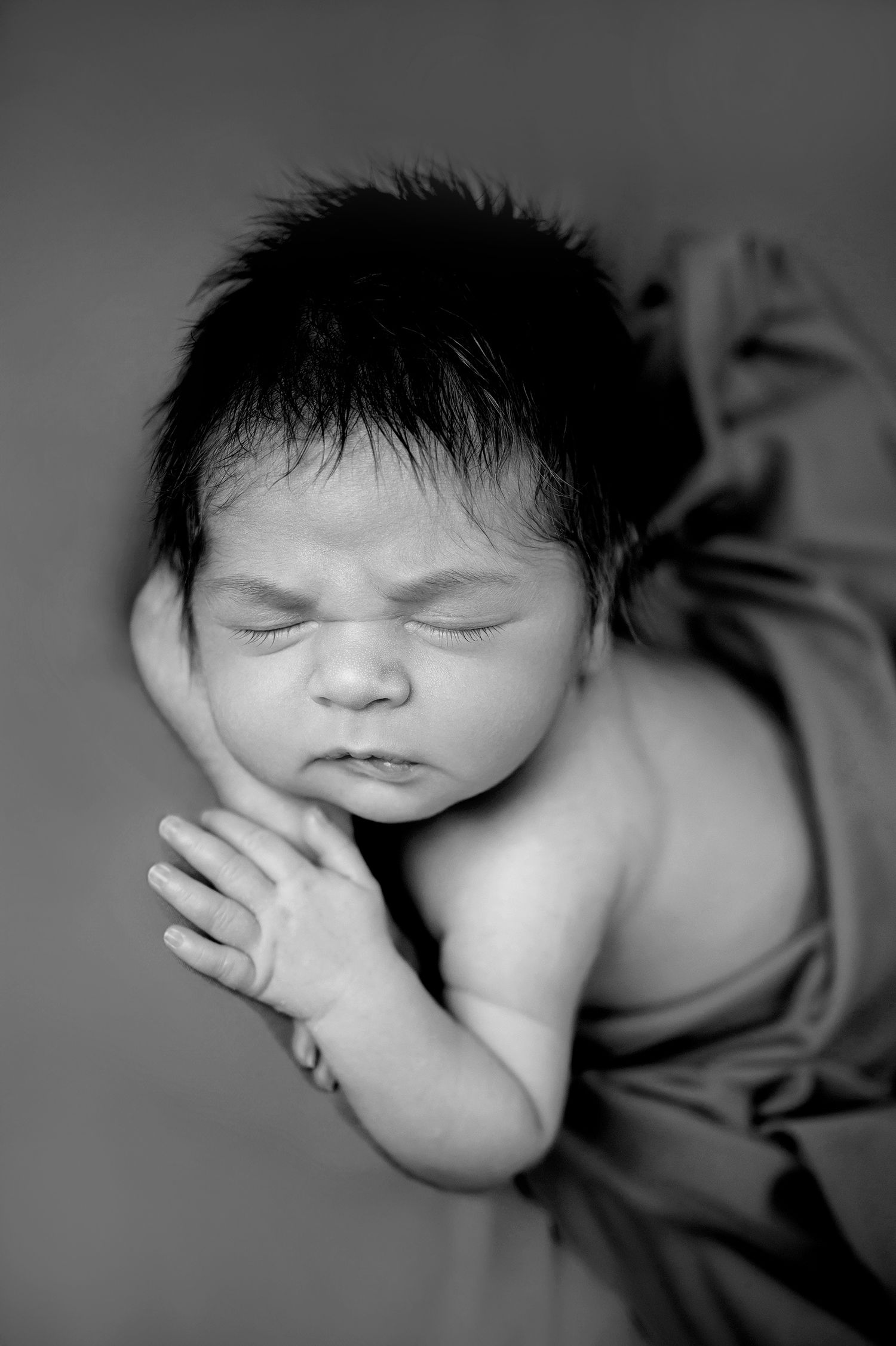 Artistic black and white portrait of sleeping newborn with hands clasped.