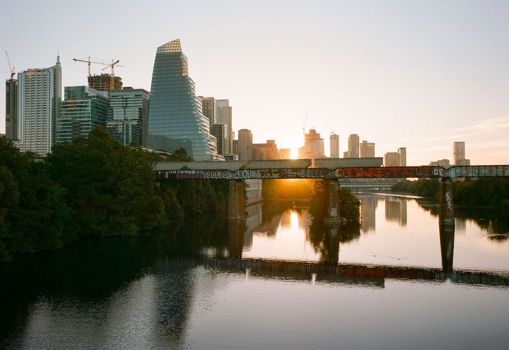 Austin downtown skyline reflected in Lady Bird Lake during sunset with warm orange glow.