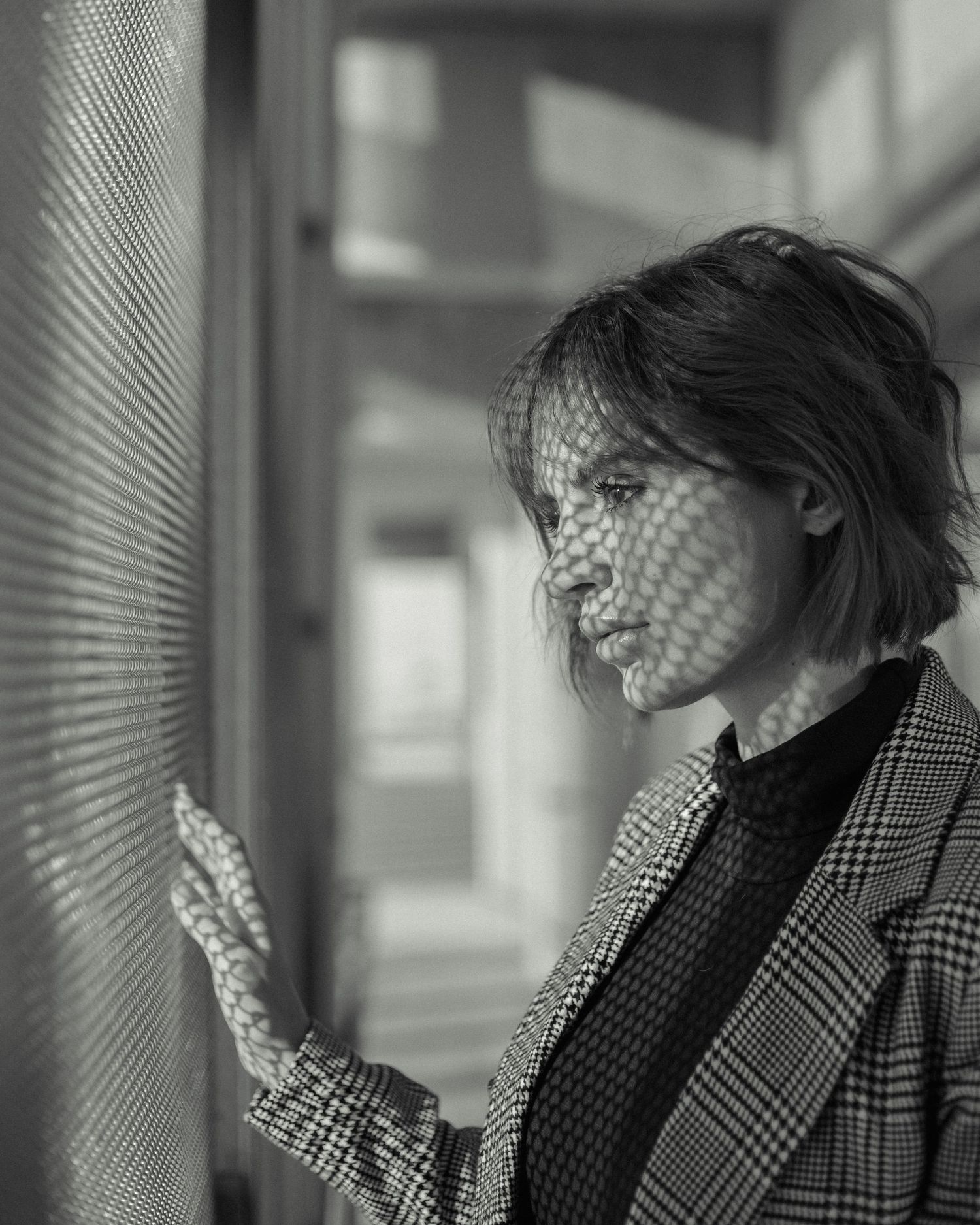 Artistic black and white portrait with shadow patterns through venetian blinds.
