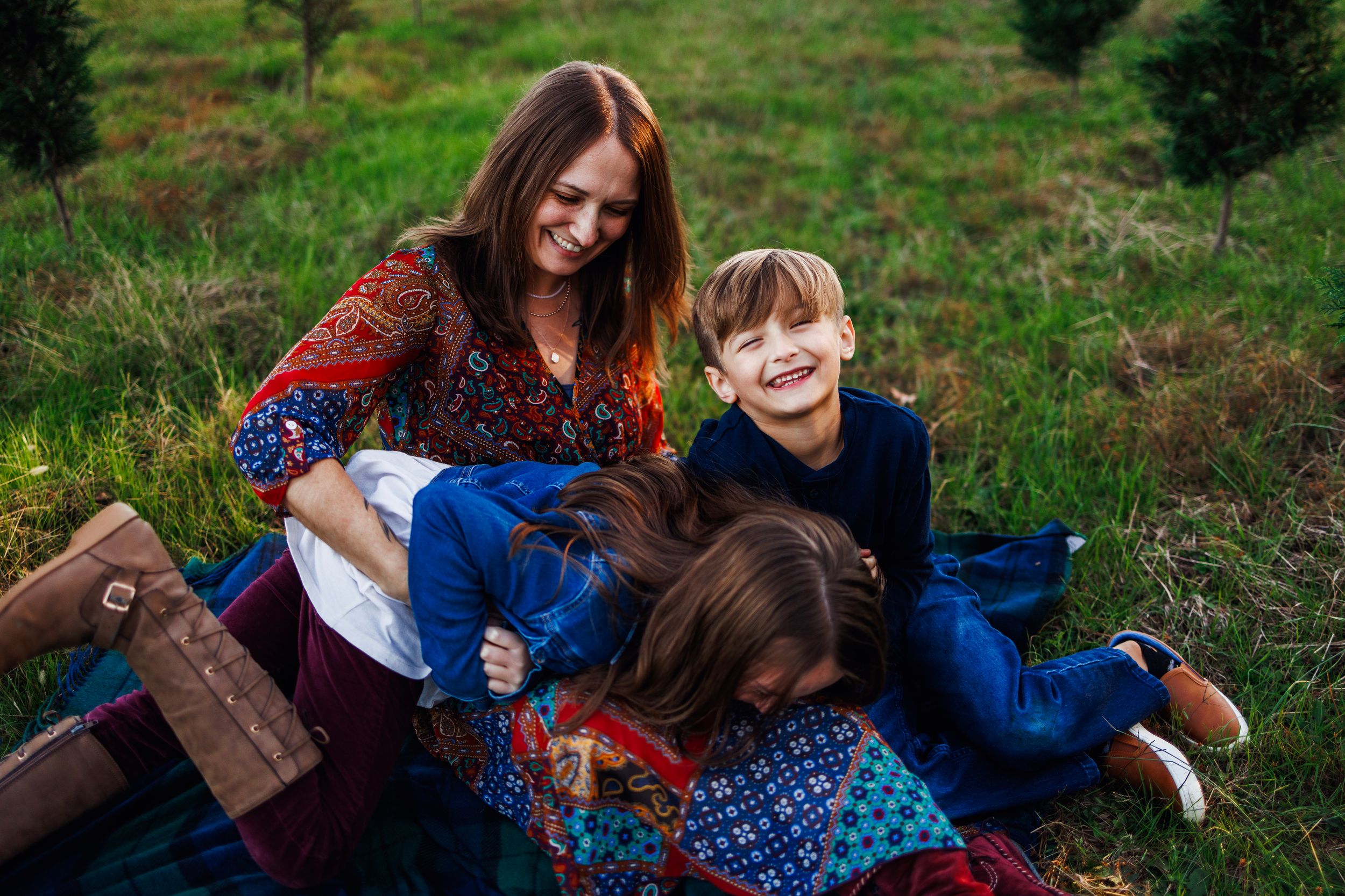 A family relaxes together on a colorful patchwork quilt spread out on green grass during an autumn day.