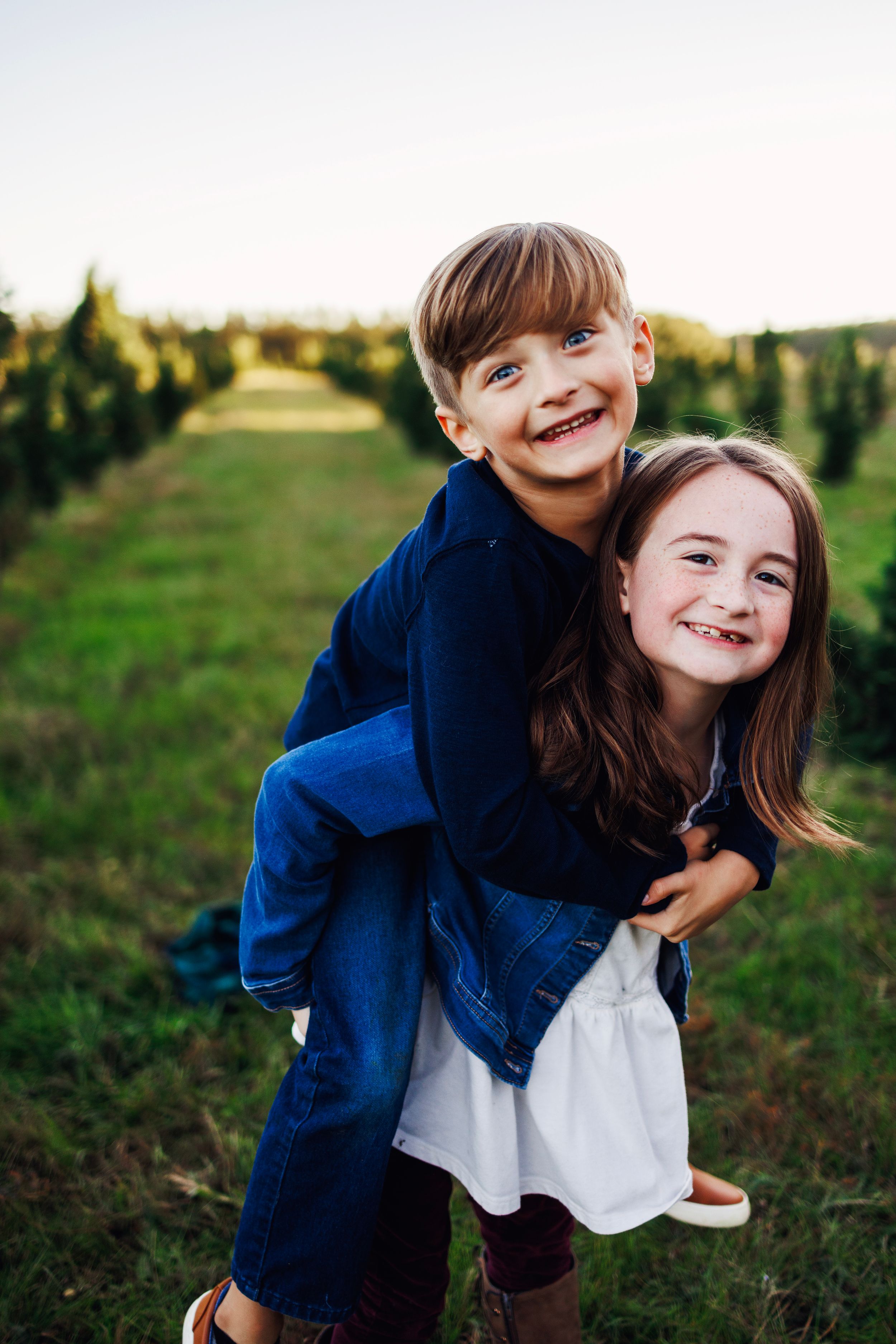 Two children wearing navy and white outfits share joyful embraces while playing outdoors in a grassy field at sunset.