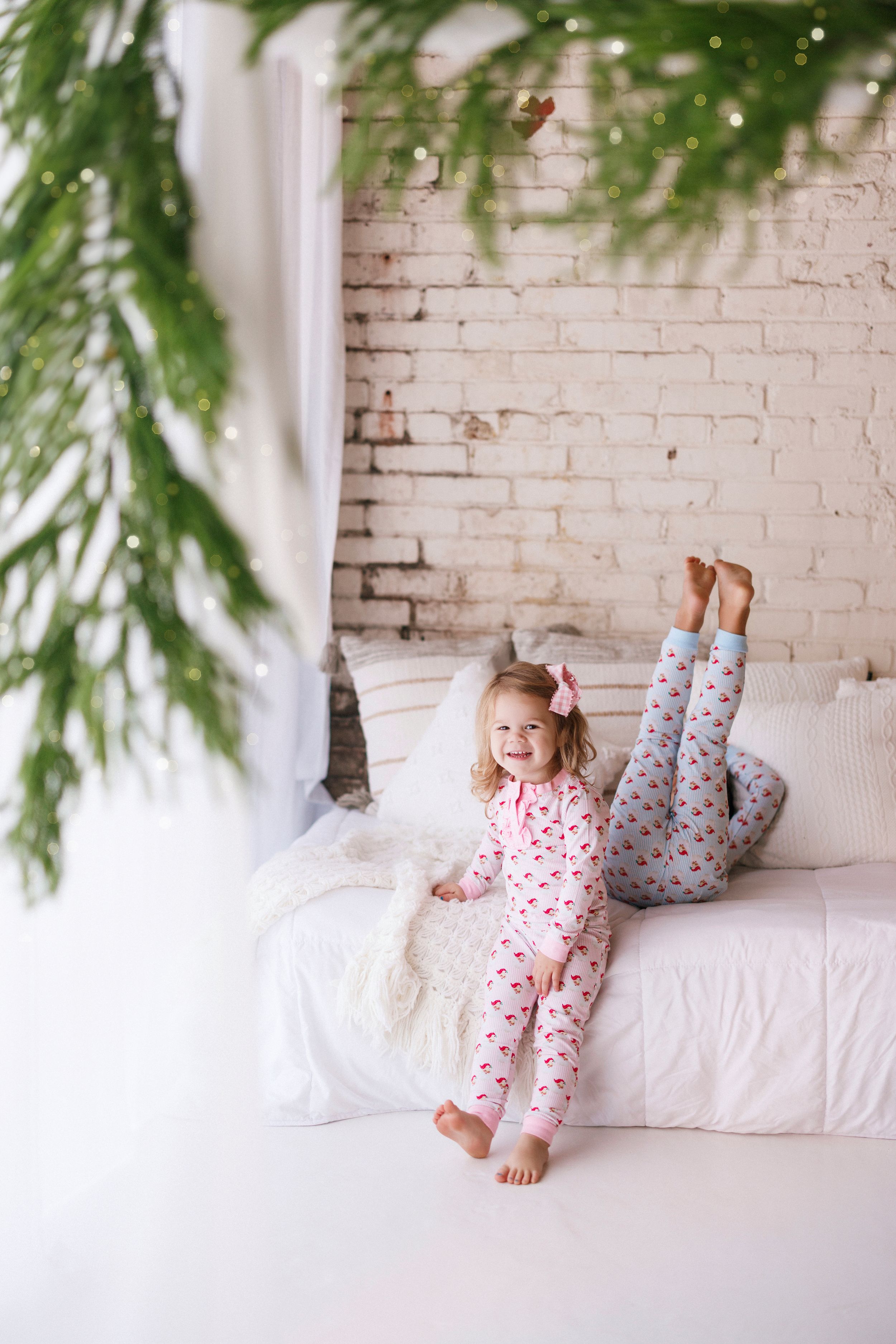 A series of photos showing a child in festive holiday pajamas lying on a white couch with evergreen branches overhead.