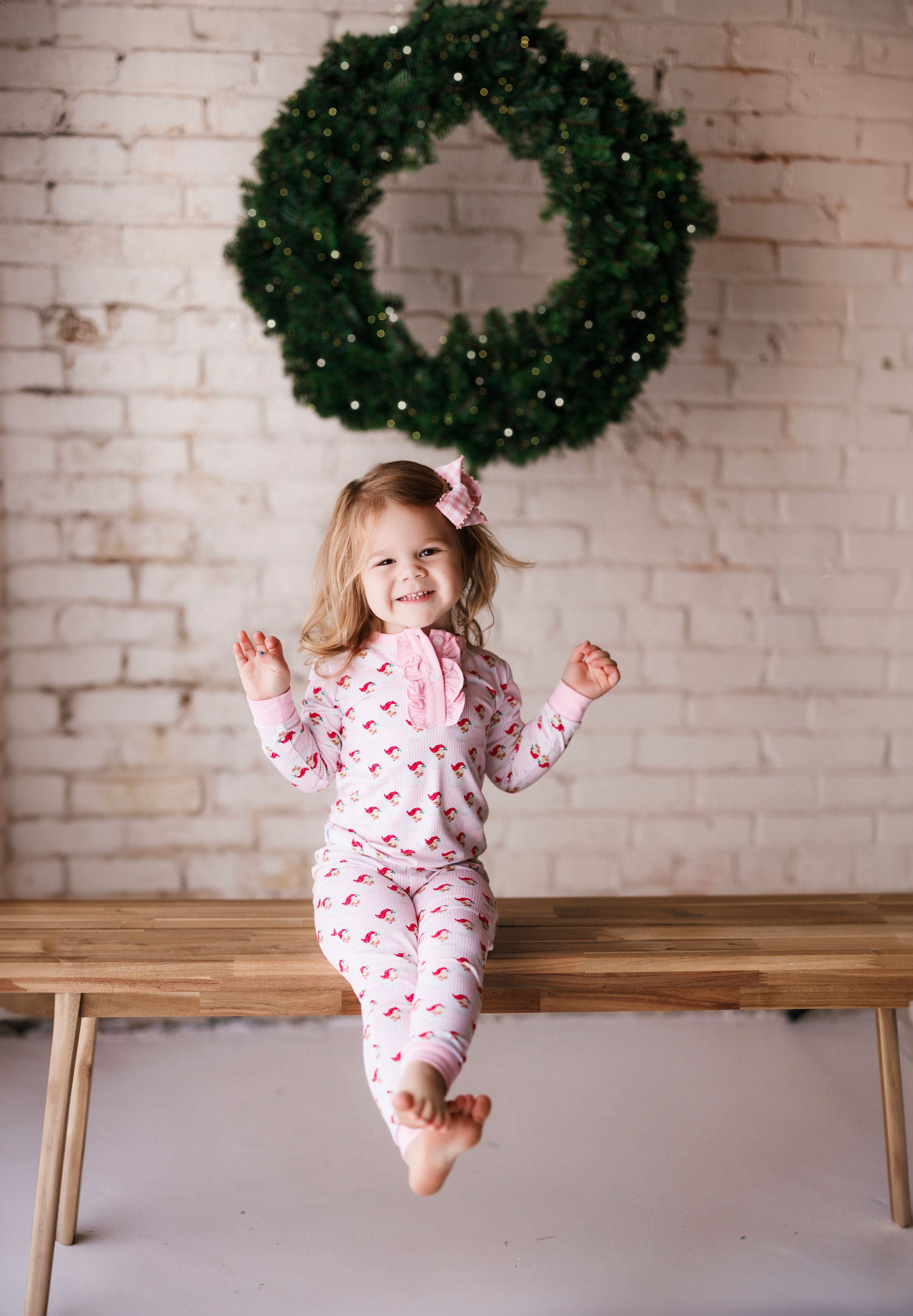 A series of five progressive photos showing a child in pink pajamas playing and posing on a wooden bench with wreaths behind.