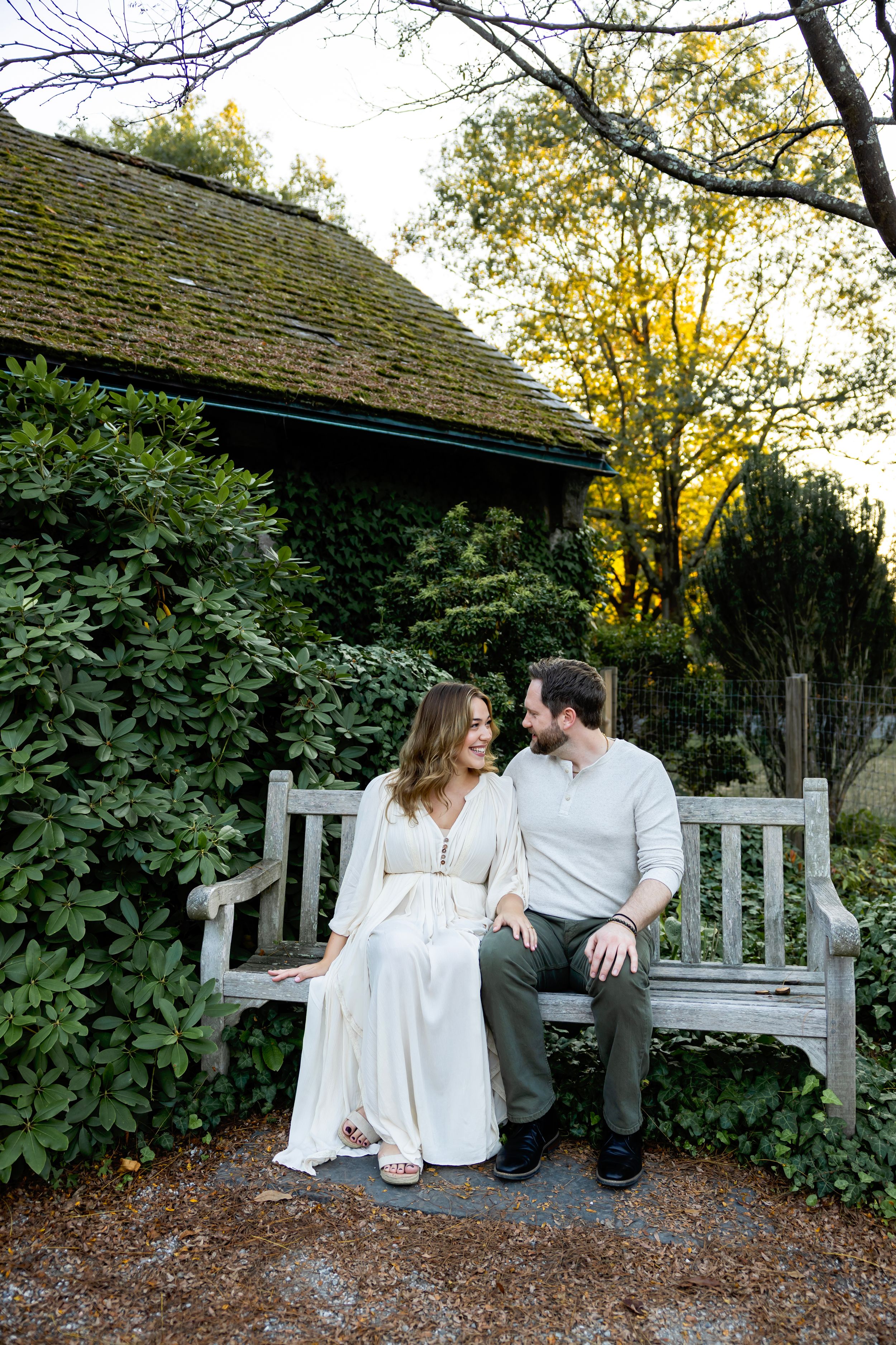 A couple shares an intimate moment while sitting together on a white garden bench at sunset.