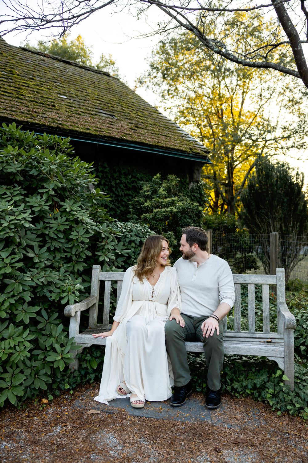 A couple shares an intimate moment while sitting together on a white garden bench at sunset.