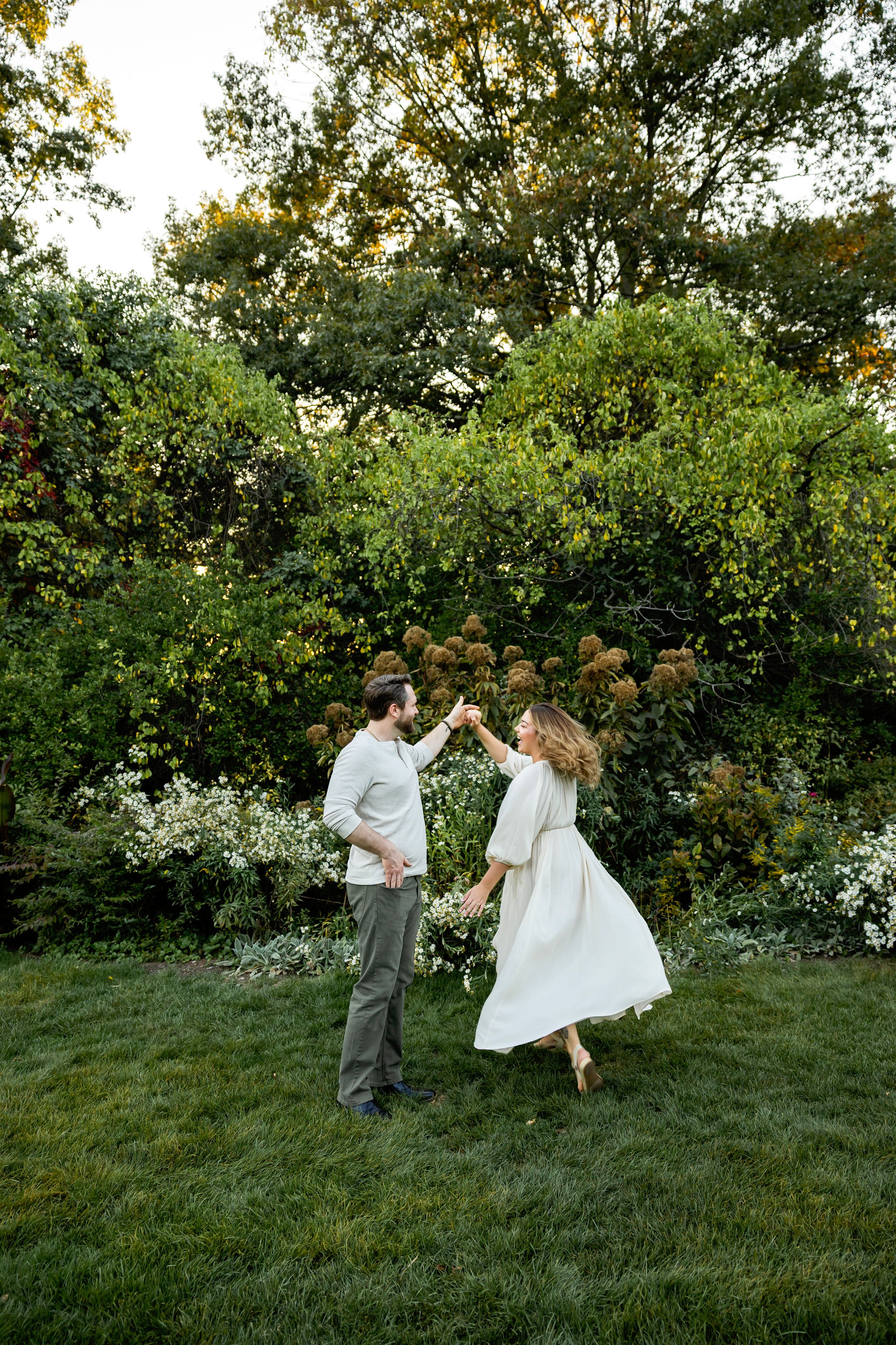 Two people share a joyful dance moment on a green lawn with lush foliage behind them.