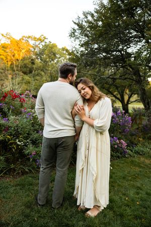 A romantic couple embraces in a garden filled with purple and red flowers during golden hour.