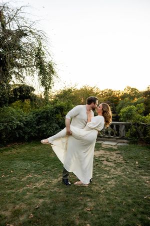 A couple performs a romantic dance lift pose in a garden during golden hour.