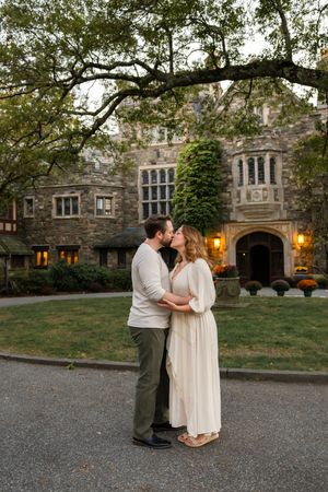 Couple shares romantic moment outside historic stone building with glowing windows at dusk.