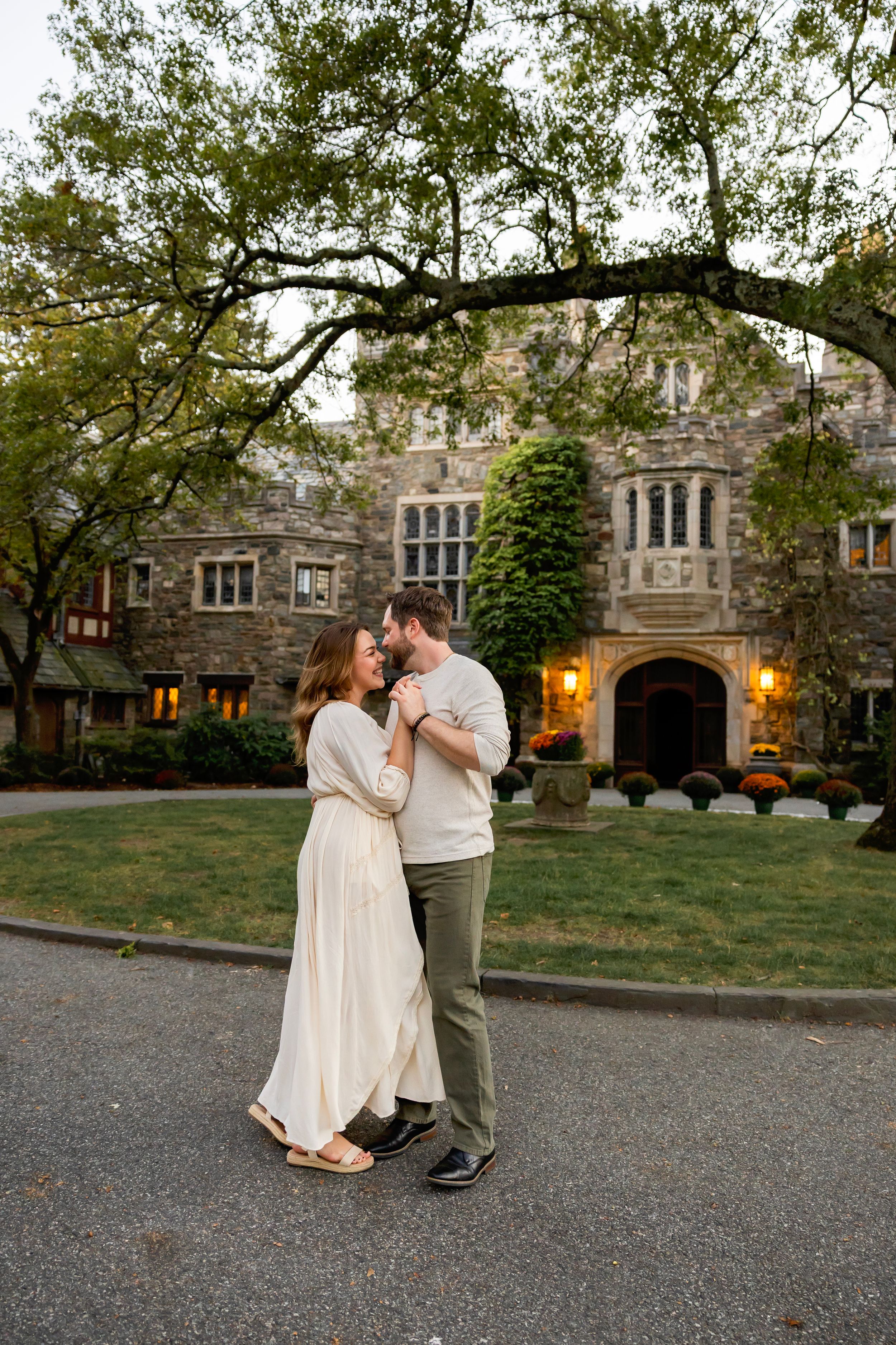 A couple dances romantically together on a stone driveway at dusk with a historic building in the background.