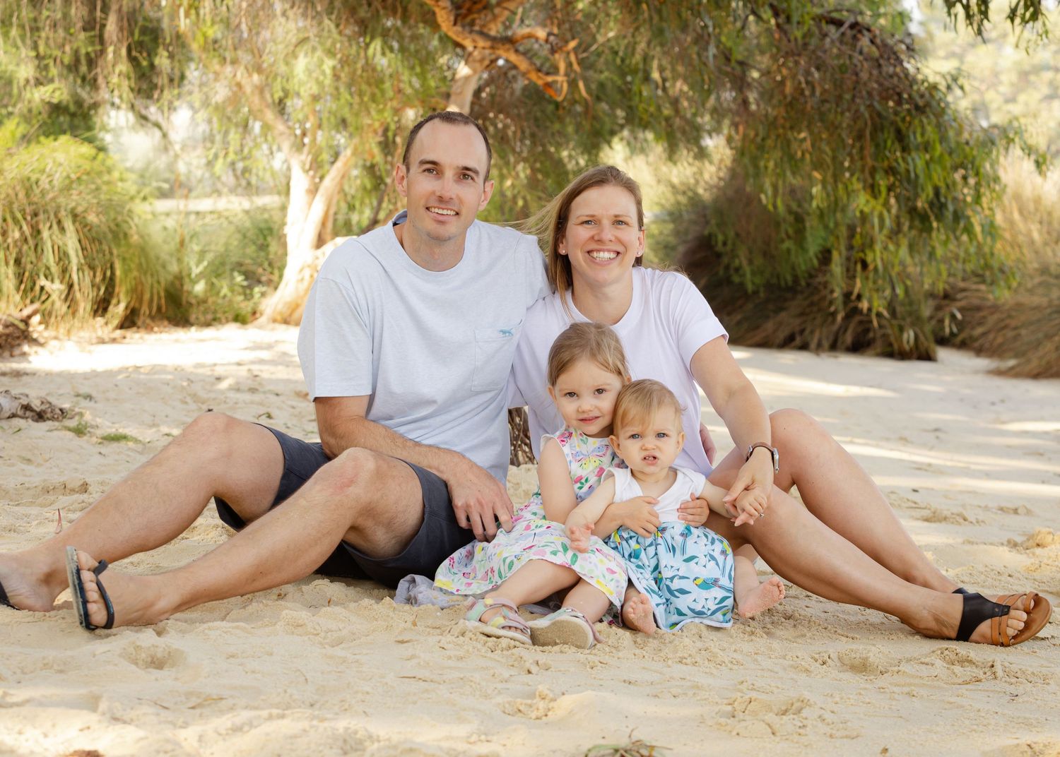 Family relaxing together on sandy beach during summer vacation photoshoot.