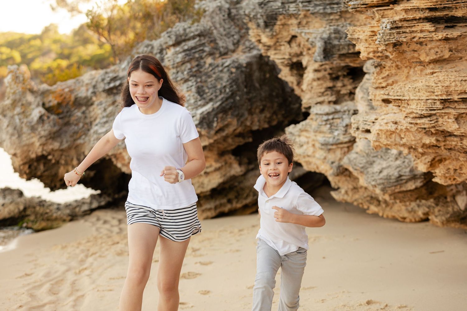 Family enjoying a sunset stroll along a rocky beach with dramatic cliffside formations in the background.