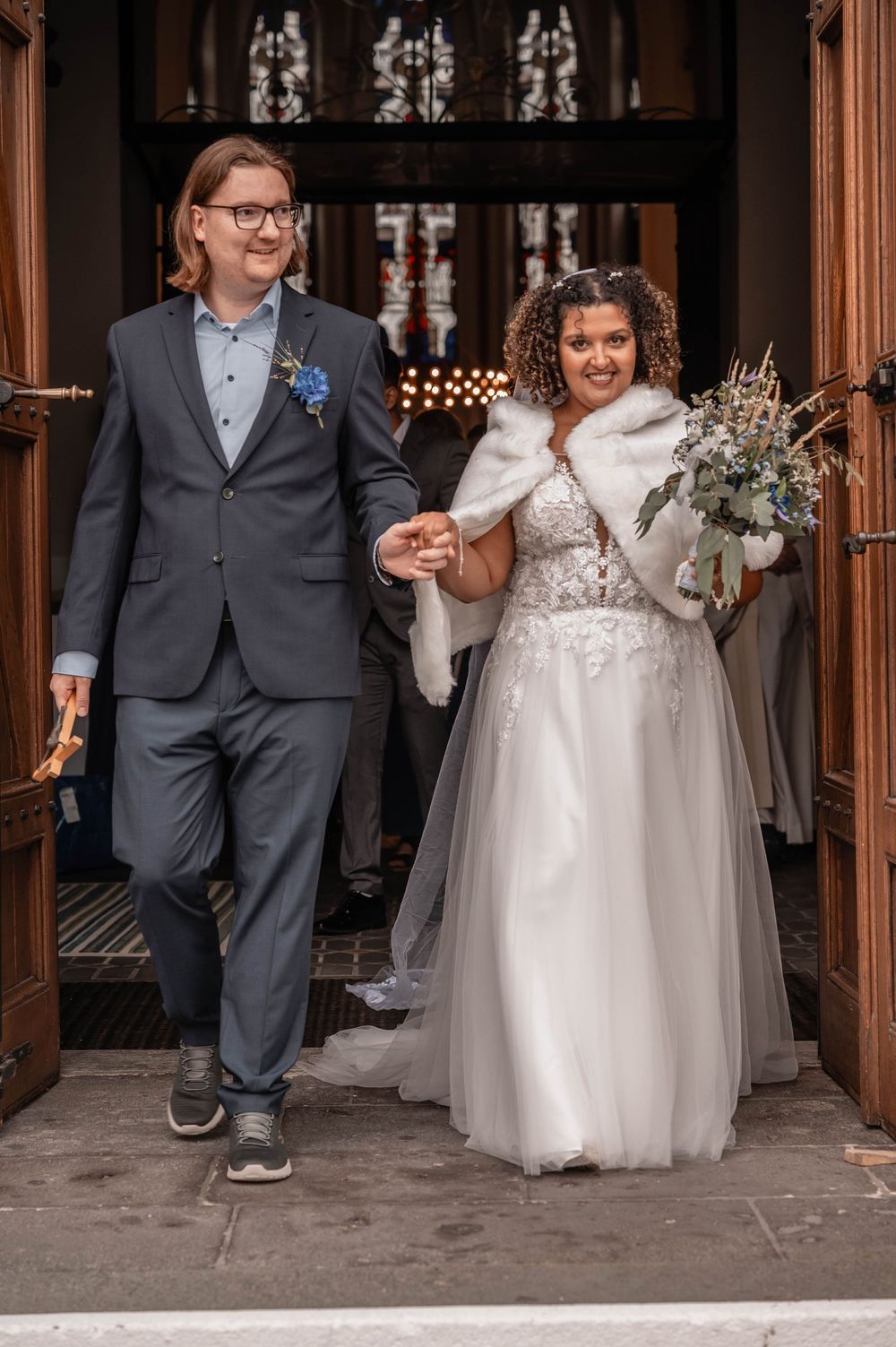 Wedding couple in gray suit and white dress walk together through a wooden paneled hallway at their celebration.