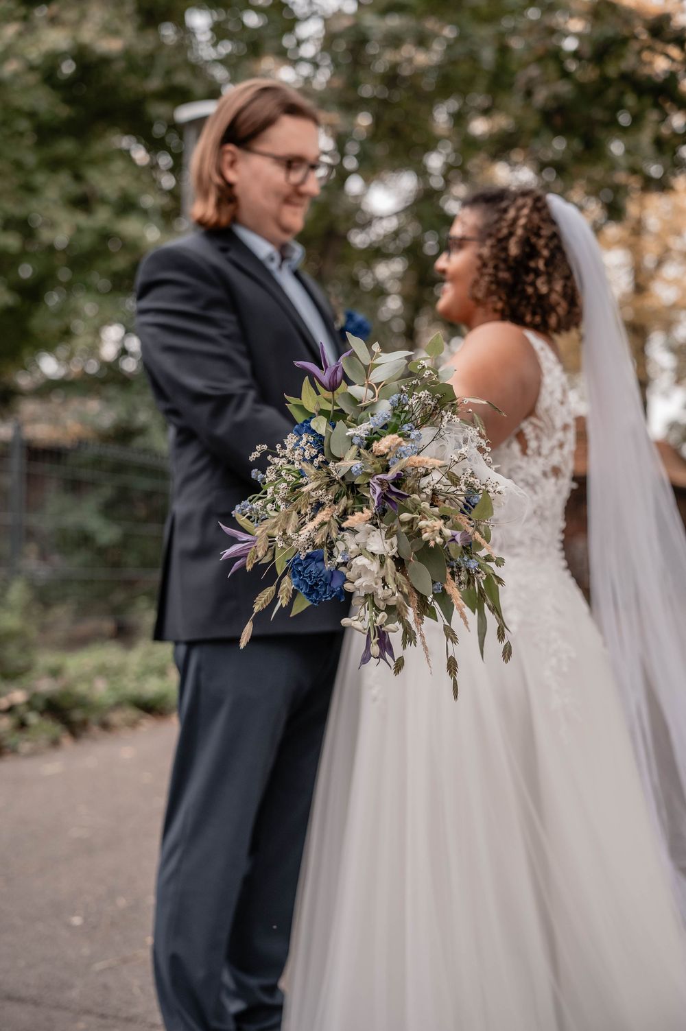 Couple shares a joyful moment outdoors during their wedding, with greenery and natural lighting in the background.