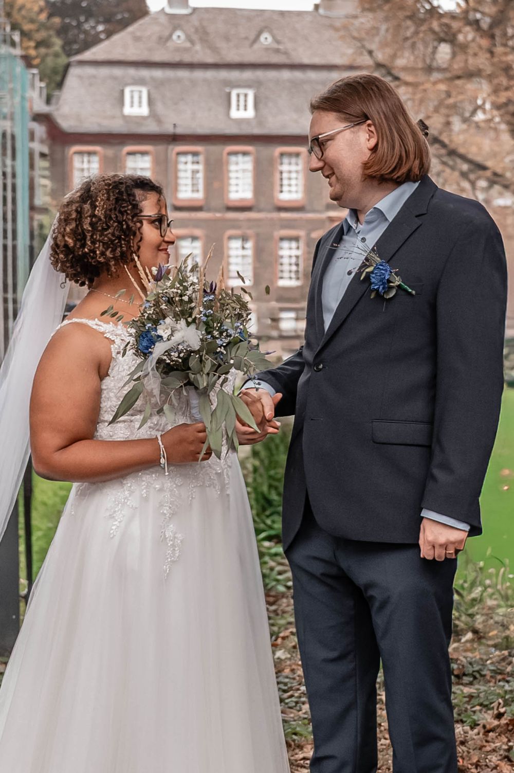 A couple shares an intimate moment during their wedding day on the grounds of a historic brick building.