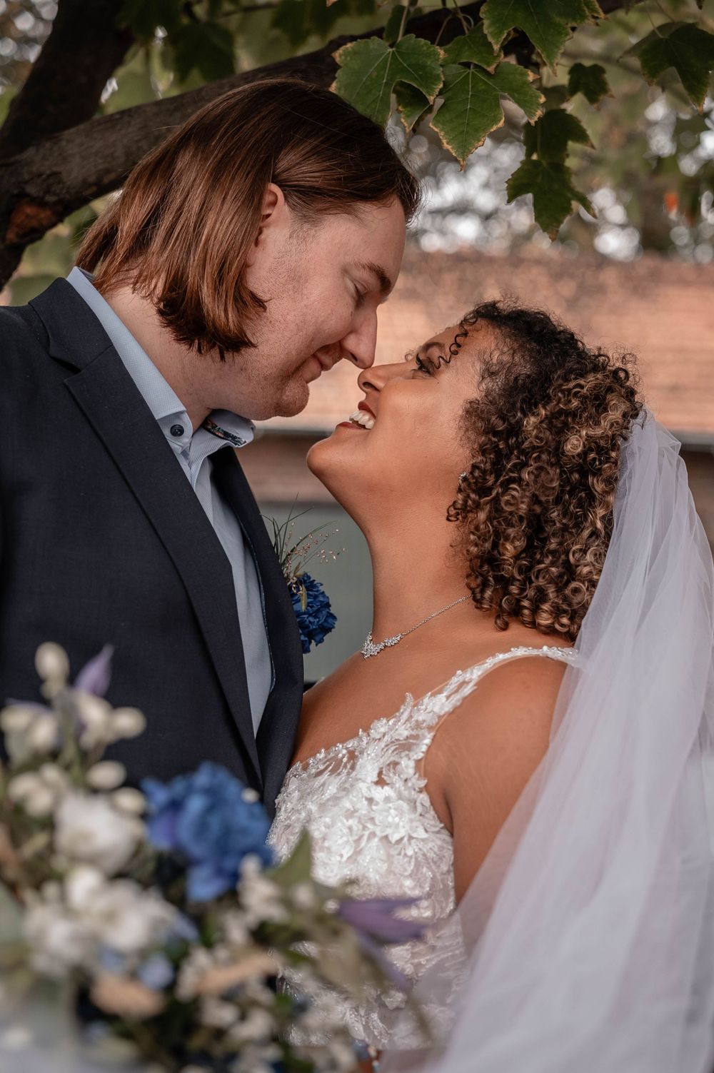 Romantic wedding moment captured under blooming cherry blossoms with white veil and blue floral accents.
