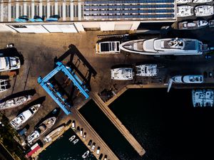 Aerial view of a luxury yacht marina with large white yachts docked alongside a blue crane at a shipyard.
