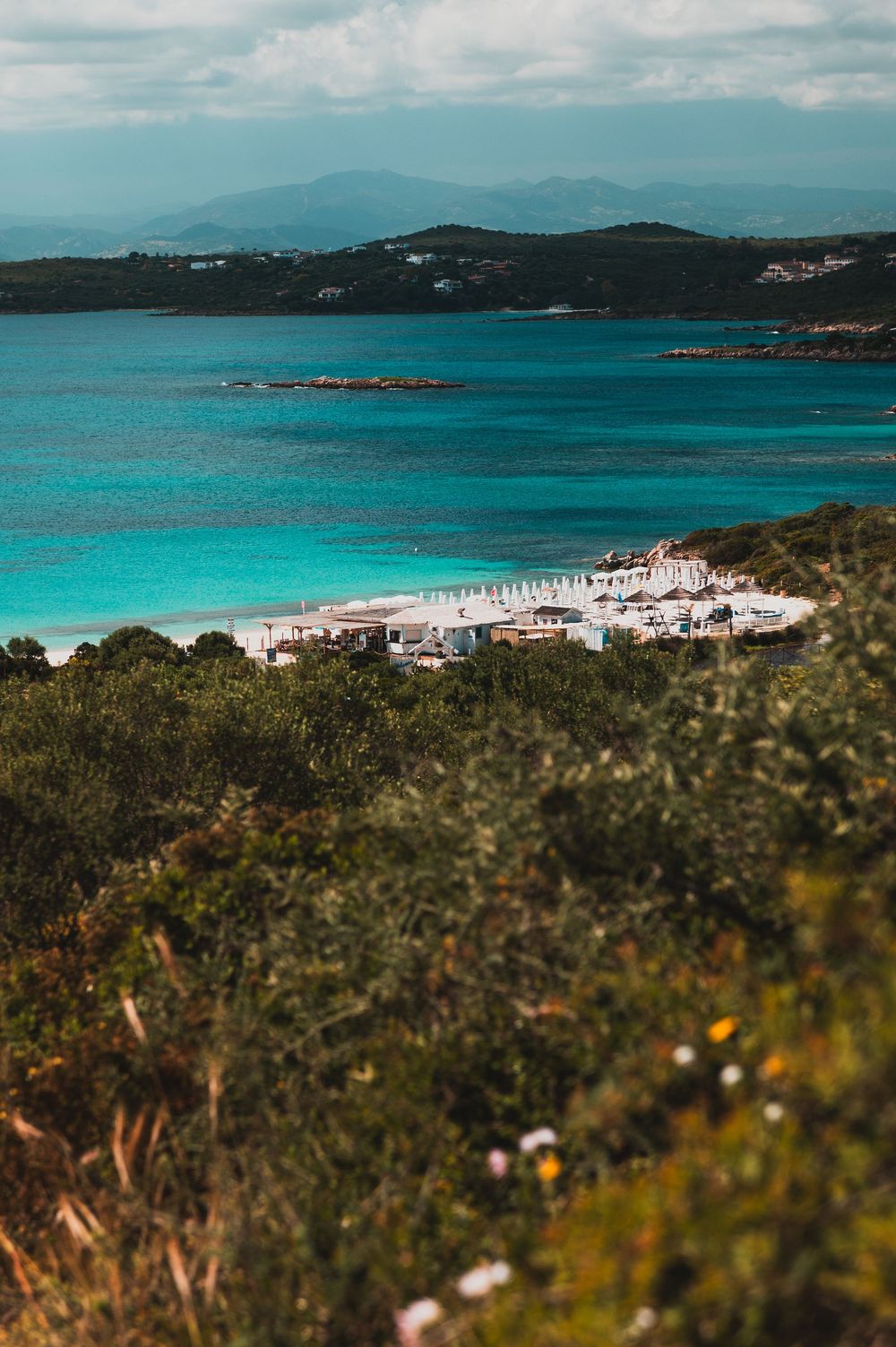 Aerial view of a turquoise Mediterranean beach resort surrounded by lush greenery and calm blue waters.