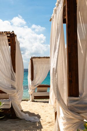 White draped canopy beach cabanas on sandy shore with turquoise ocean and blue sky backdrop.