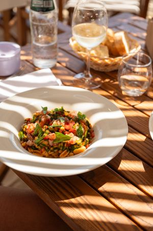 Fresh pasta salad with tomatoes, greens, and herbs served in a white bowl on a sunny outdoor restaurant table.