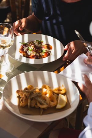 Server presenting elegant seafood dishes including calamari with lemon at a fine dining restaurant.