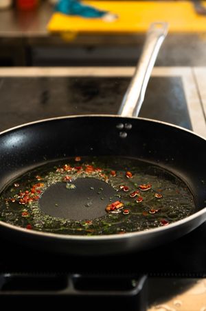 Black non-stick frying pan with sizzling olive oil and red chili flakes on an induction stovetop.