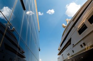Two luxury yachts docked side by side under a blue sky, viewed from below showing sleek hulls and rigging.
