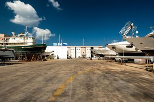 Boats and yachts stored in a dry dock shipyard facility under a bright blue sky with white clouds.