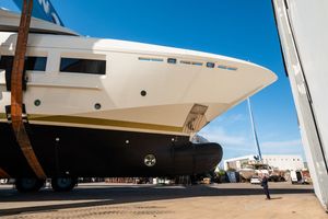 Large luxury yacht under construction in a shipyard, showcasing its sleek hull and multi-deck design against a clear blue sky.