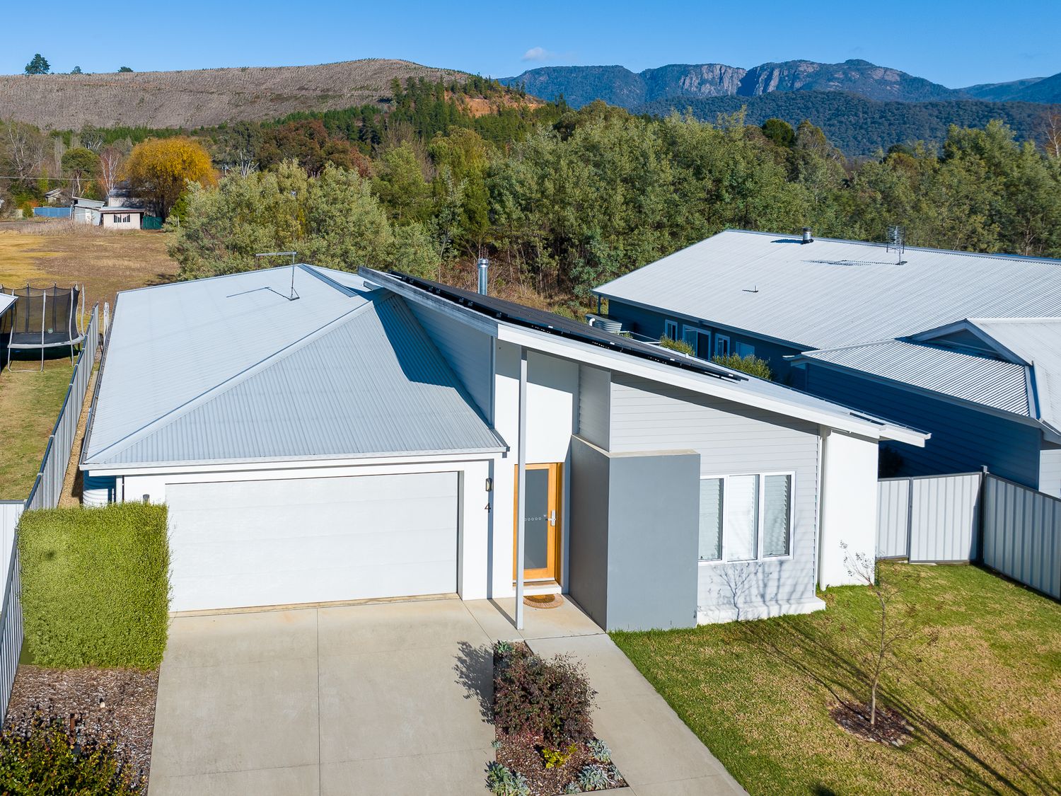 Contemporary grey rendered home with double garage and mountain views under partly cloudy skies.