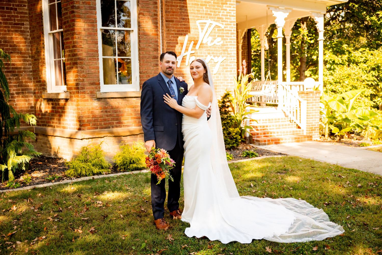 Romantic wedding couple poses together in front of a rustic brick building during golden hour sunset.