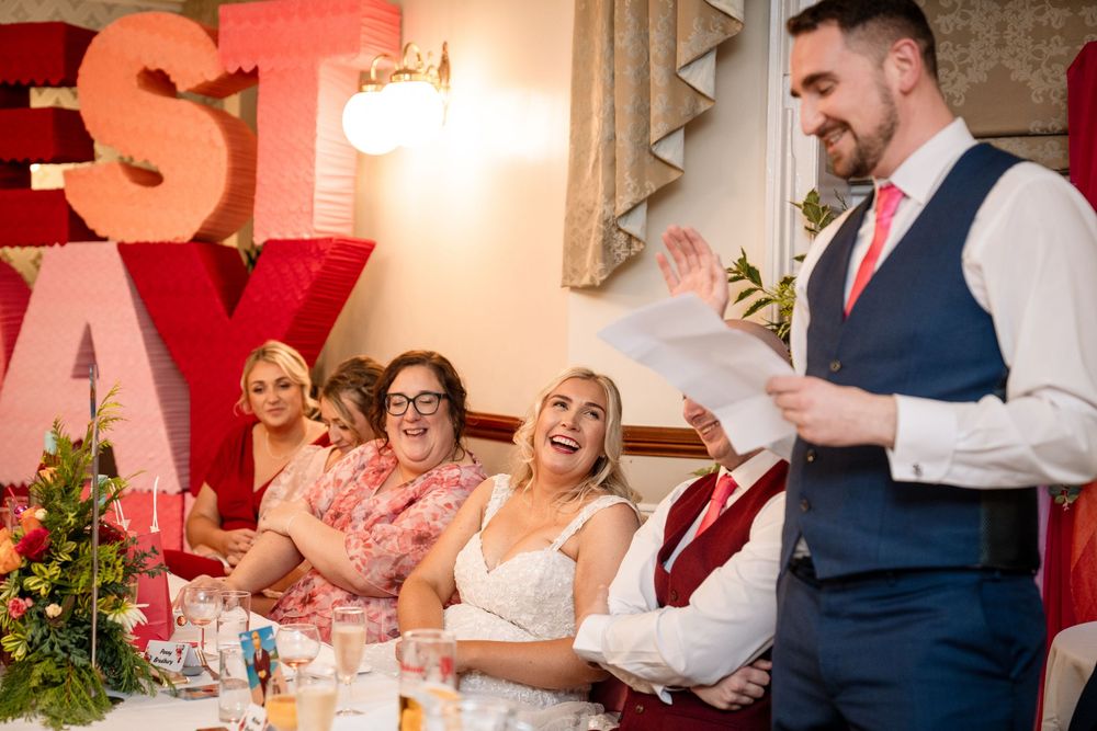 Wedding guests seated at tables during reception share joyful moments in a warmly lit venue with red accents.