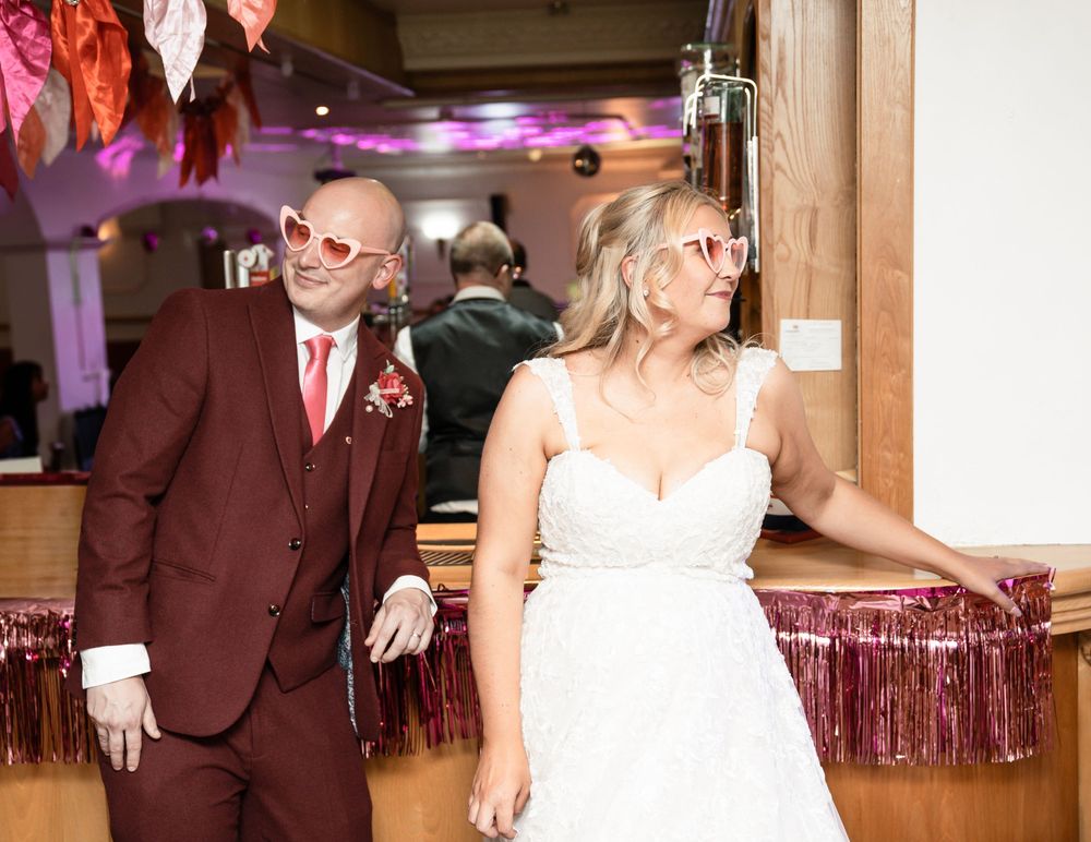 A couple in burgundy and white attire share their first dance at a wedding reception with purple lighting.