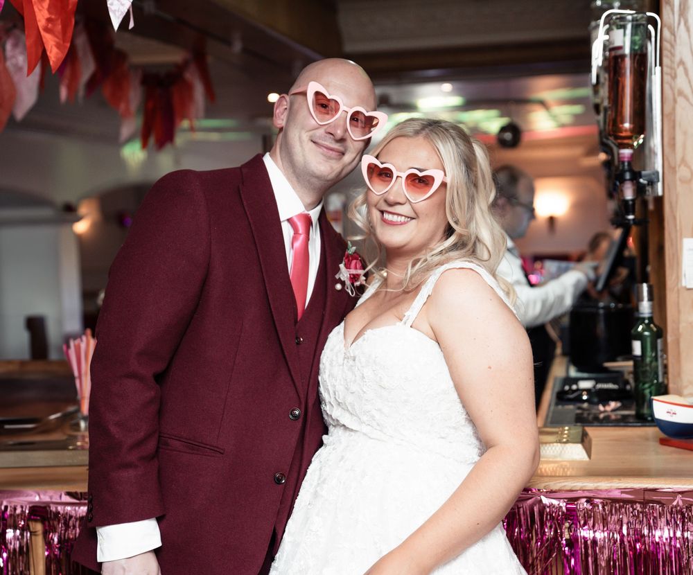 A wedding couple shares a joyful moment in burgundy and white attire at an indoor reception venue.