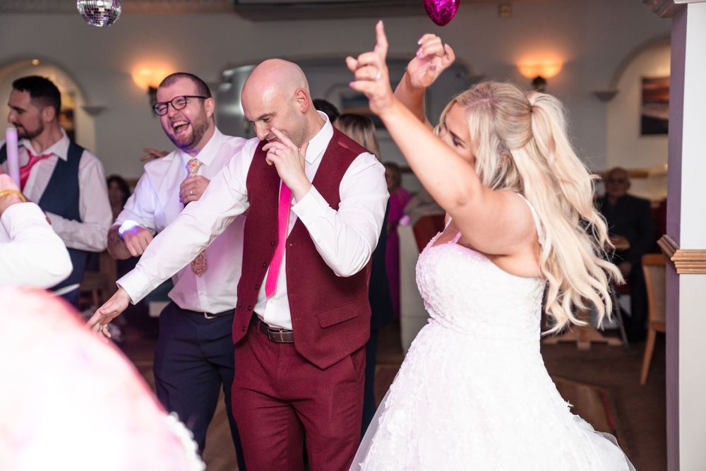 Wedding party dances and celebrates together during reception in an indoor venue with warm lighting.