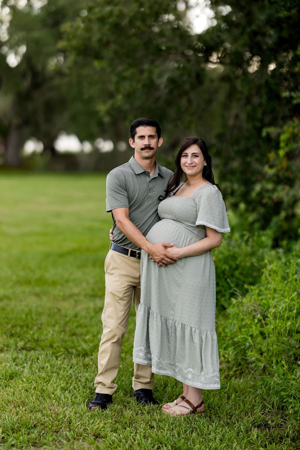 A couple poses together outdoors in a grassy field during a maternity photo session.