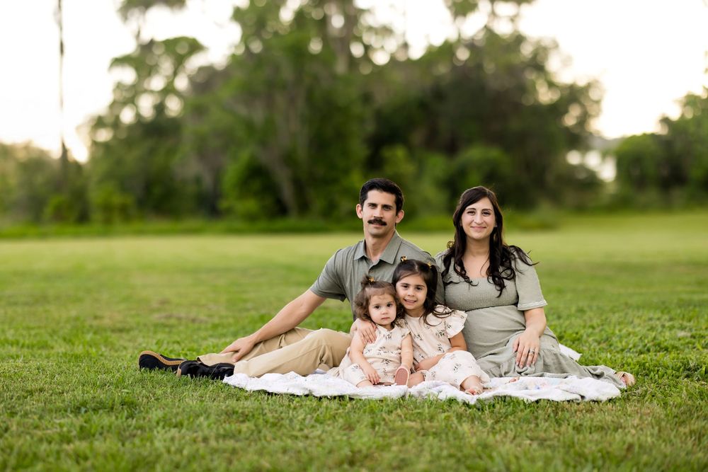 Family relaxes together on blanket in green grass during outdoor photo session.