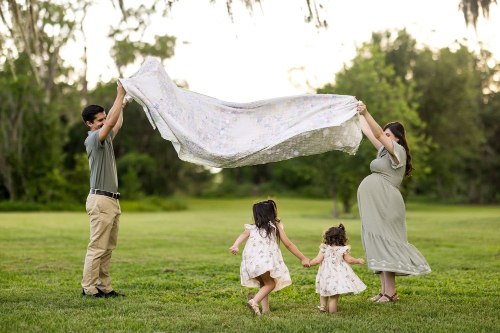 People running and playing with white sheets in a grassy field during golden hour.