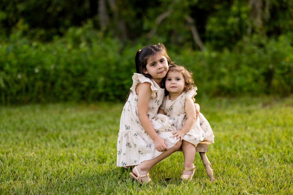 A child in a floral dress plays joyfully on a grassy lawn during a sunny summer day.
