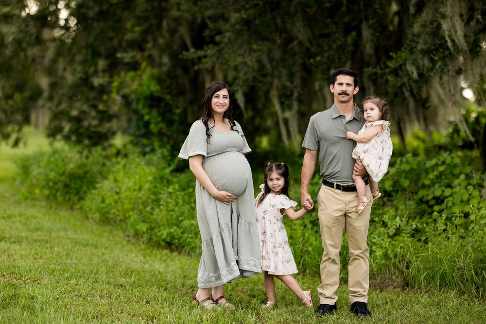 A family stands together outdoors in a lush green setting wearing coordinated casual outfits.