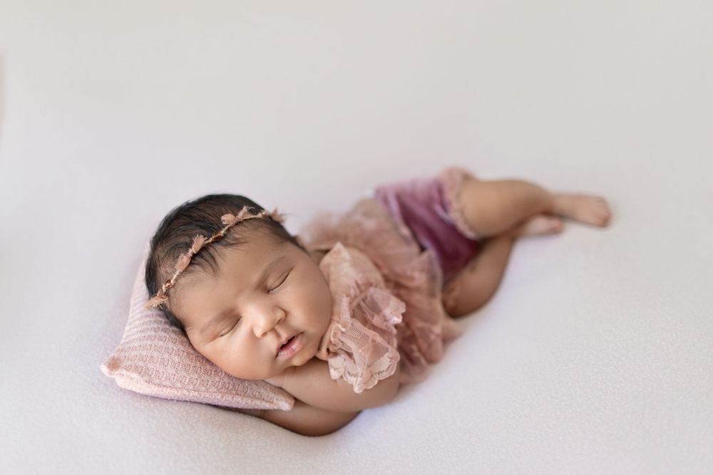 Peaceful sleeping newborn baby wearing pink swaddle wrap rests on soft white blanket during professional photo session.