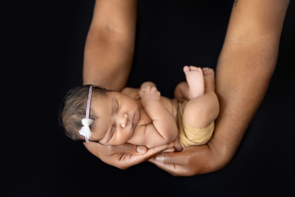 Close-up of tiny newborn baby feet being gently held in adult hands against black background.