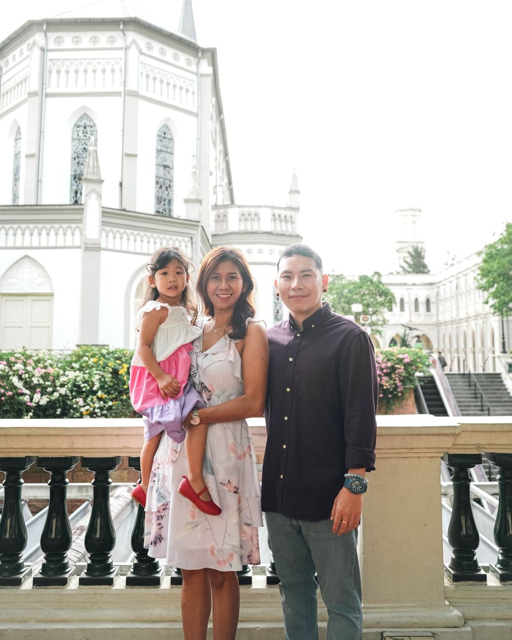 A family stands together on a balcony with a white church building visible in the background.